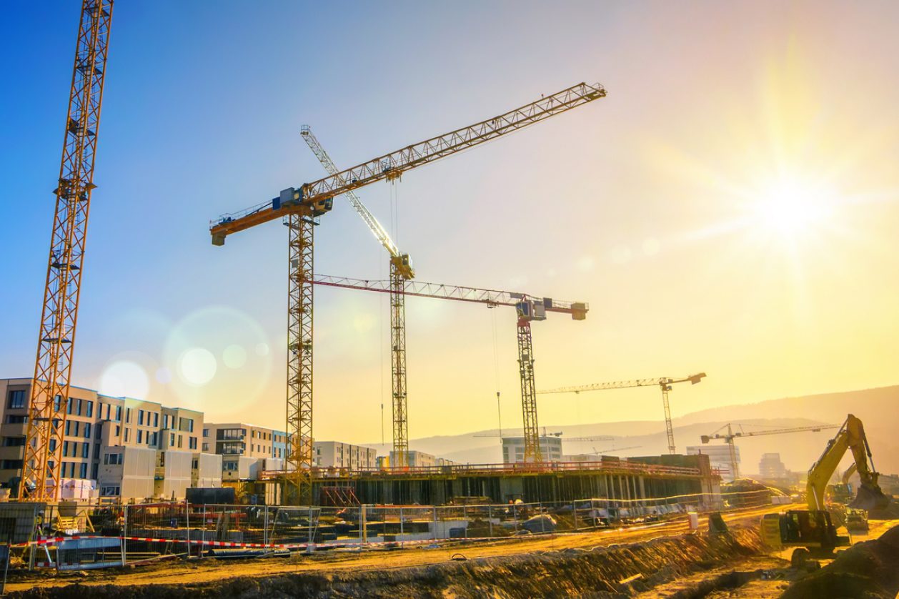 Large construction site including several cranes, with clear sky and the sun, construction consultant